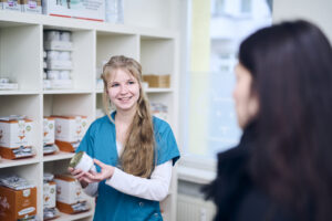 Mitarbeiterin einer Tierarztpraxis berät eine Kundin zur Tierernährung und zeigt ein Futtermittel vor einem Regal mit Tierfutterprodukten.