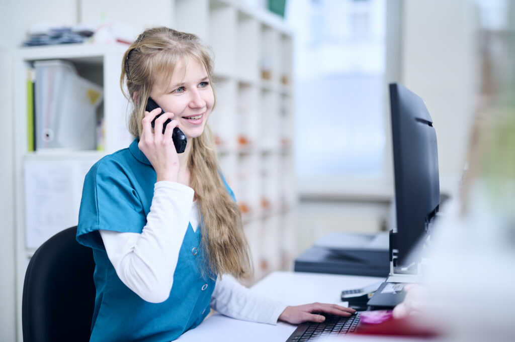 Mitarbeiterin einer Tierarztpraxis telefoniert am Empfang und arbeitet am Computer.