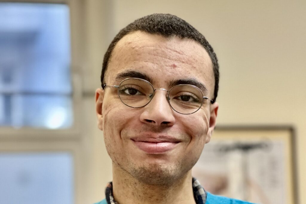 Porträt eines lächelnden Mitarbeiters einer Tierarztpraxis mit runder Brille in einem Innenraum.